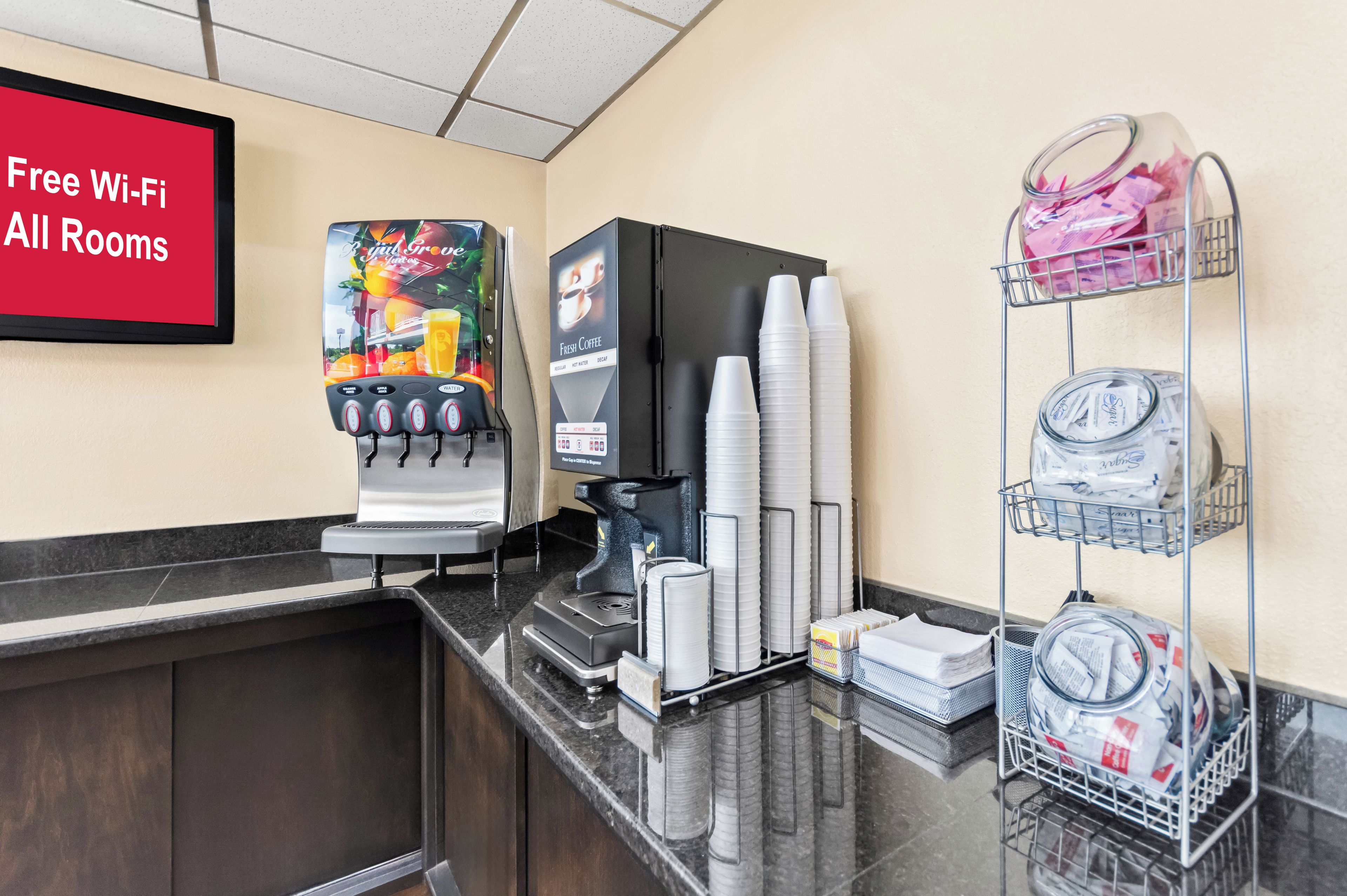 A hotel reception area with a coffee machine, a menu board, and a stack of disposable cups.