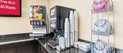 A hotel reception area with a coffee machine, a menu board, and a stack of disposable cups.
