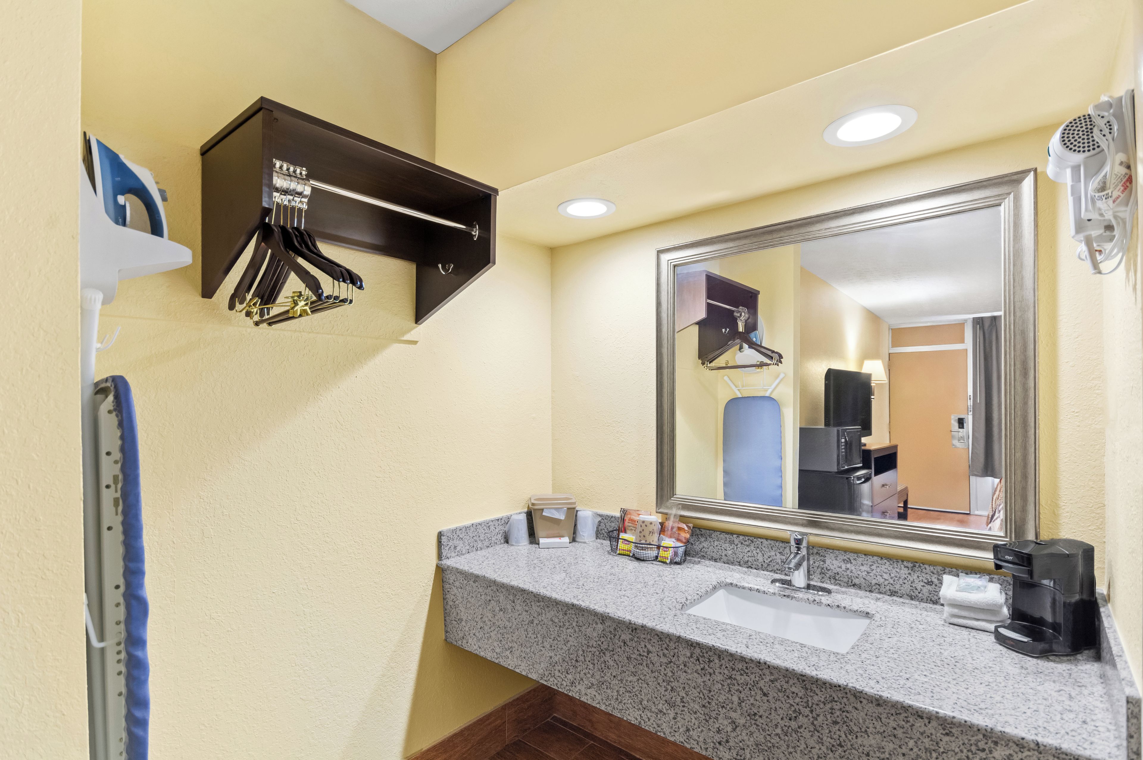 A hotel bathroom with a granite countertop, a sink, a mirror, a hairdryer, and a towel rack.