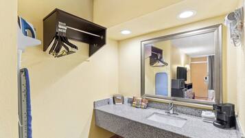 A hotel bathroom with a granite countertop, a sink, a mirror, a hairdryer, and a towel rack.