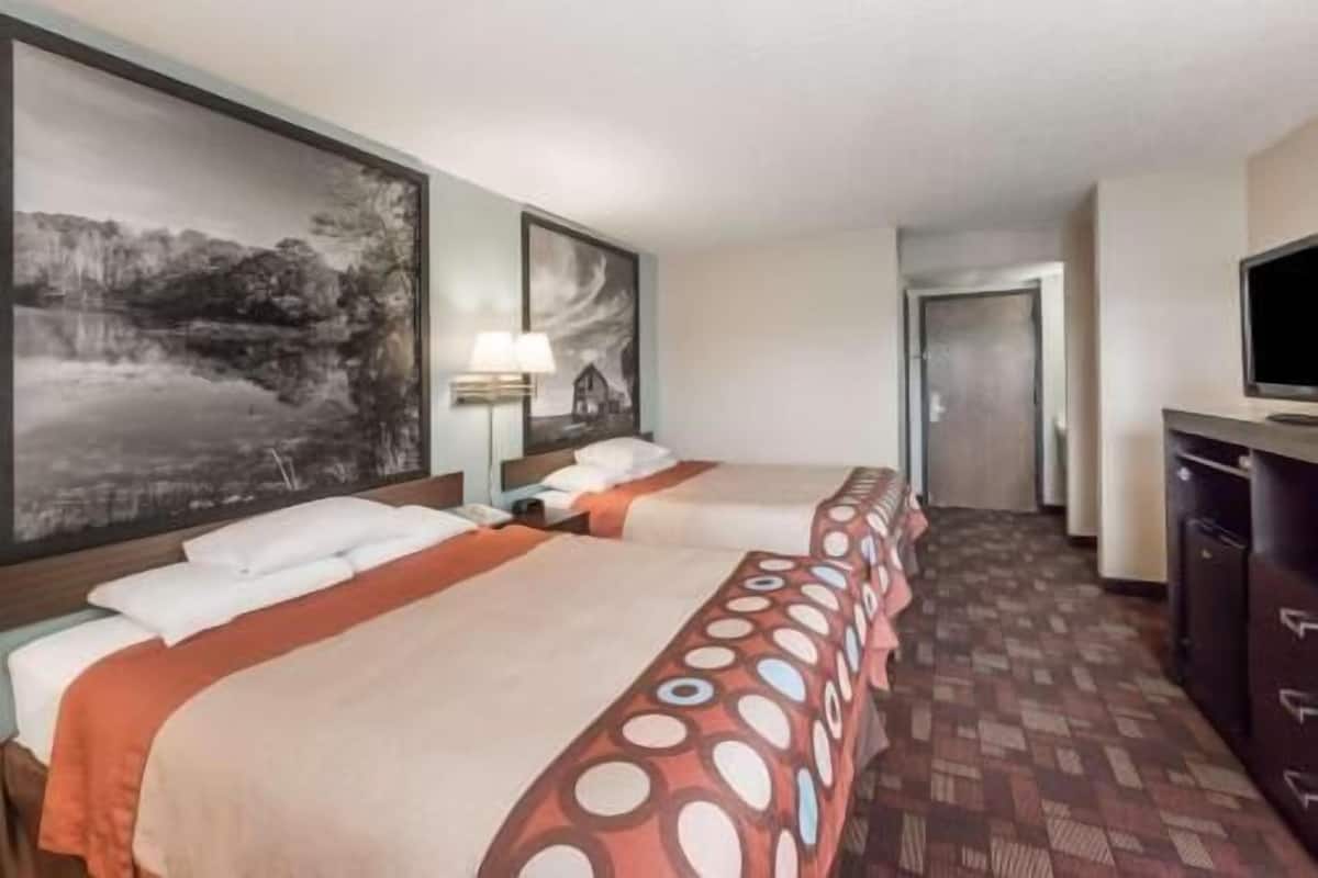 A hotel room with two beds, a large painting on the wall, a desk with a lamp, and a television.