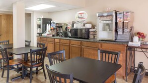 A breakfast area with tables and chairs, a refrigerator, a microwave, and a coffee machine.