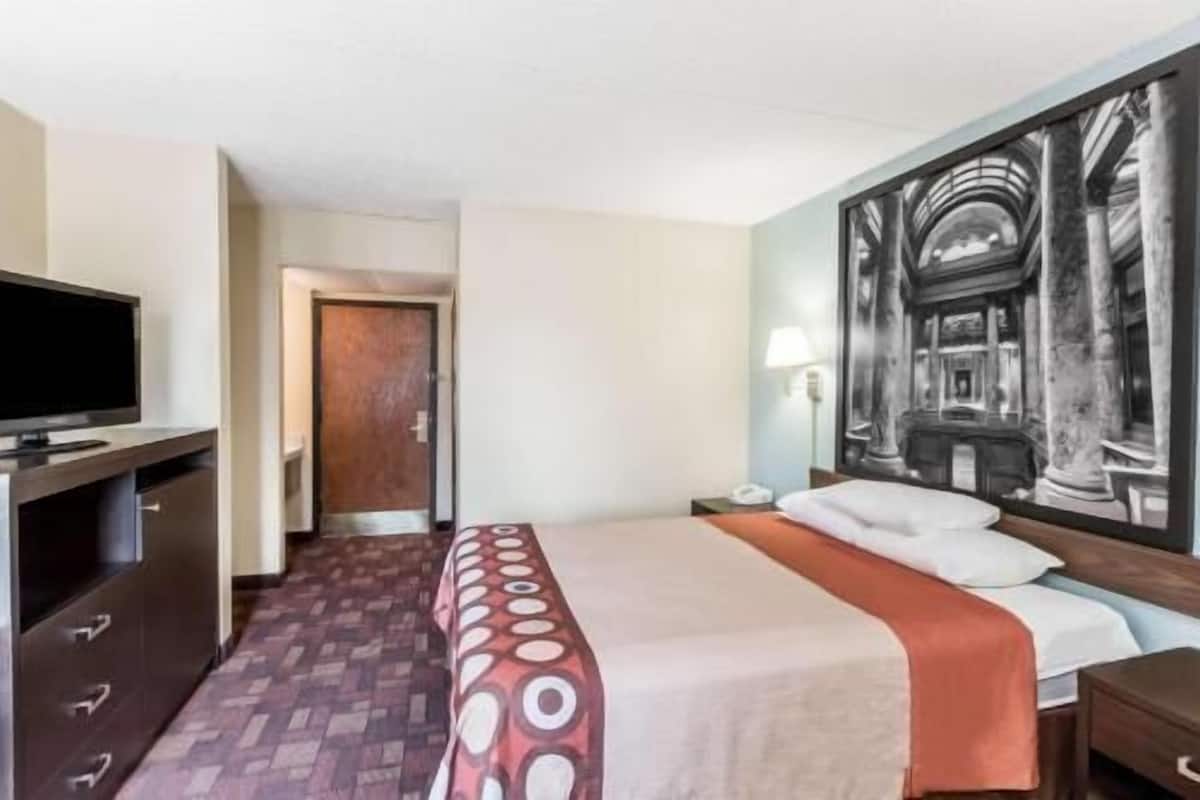 A hotel room with a bed, a television, a painting, and a door.