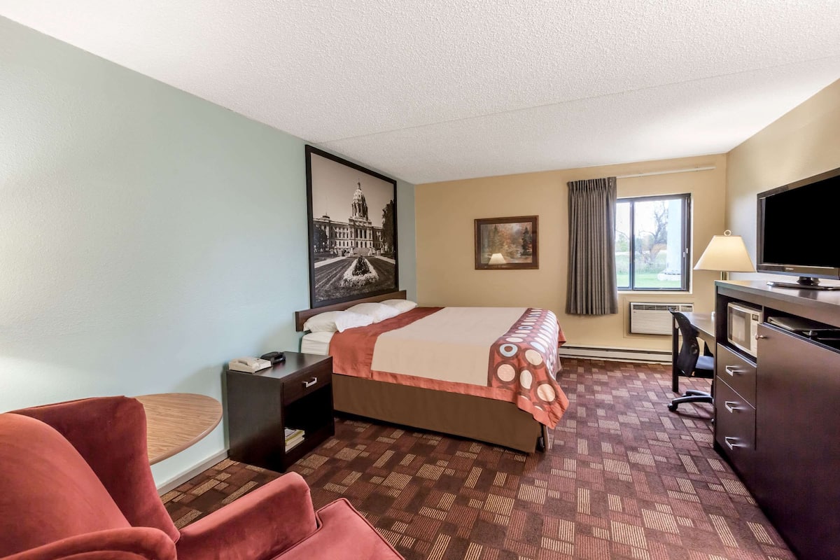 A hotel room with a bed, a desk, a chair, a TV, and a window with curtains.