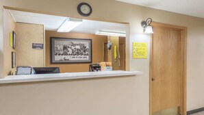 A reception desk with a clock, framed artwork, and a sign indicating check-in and check-out times.