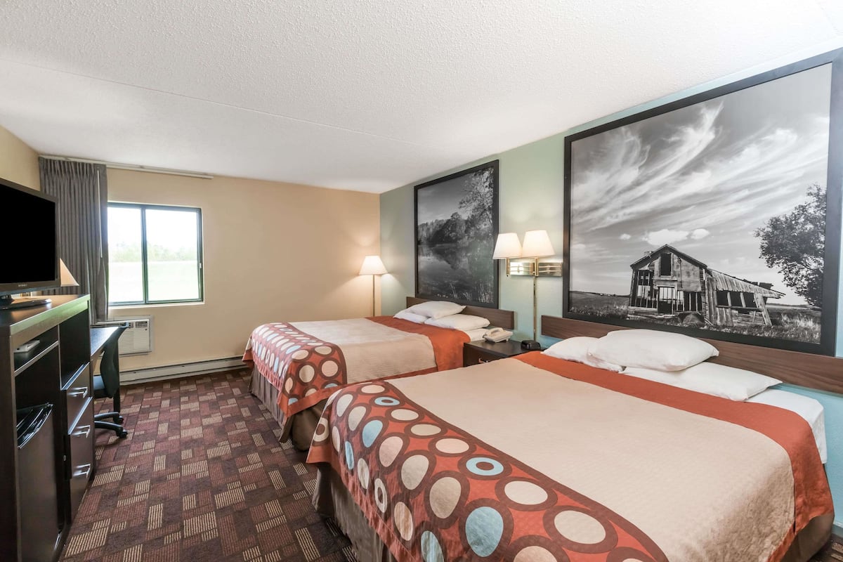 A hotel room with two beds, a desk, a TV, and a large window.