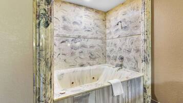 Un baño con pared de diseño tipo mármol, una bañera y zona de ducha.