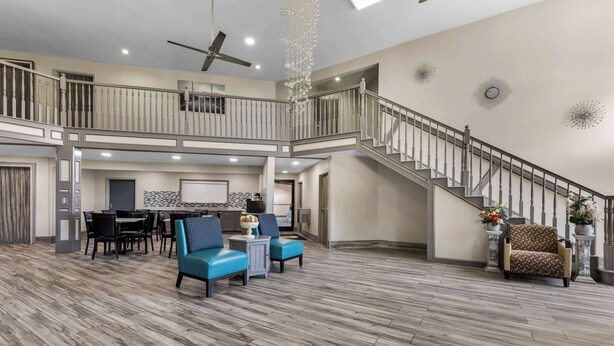 A spacious living area with a wooden floor, a dining table with chairs, a sofa, and a staircase with a railing. - Super 8 by Wyndham Dickson (Dickson)