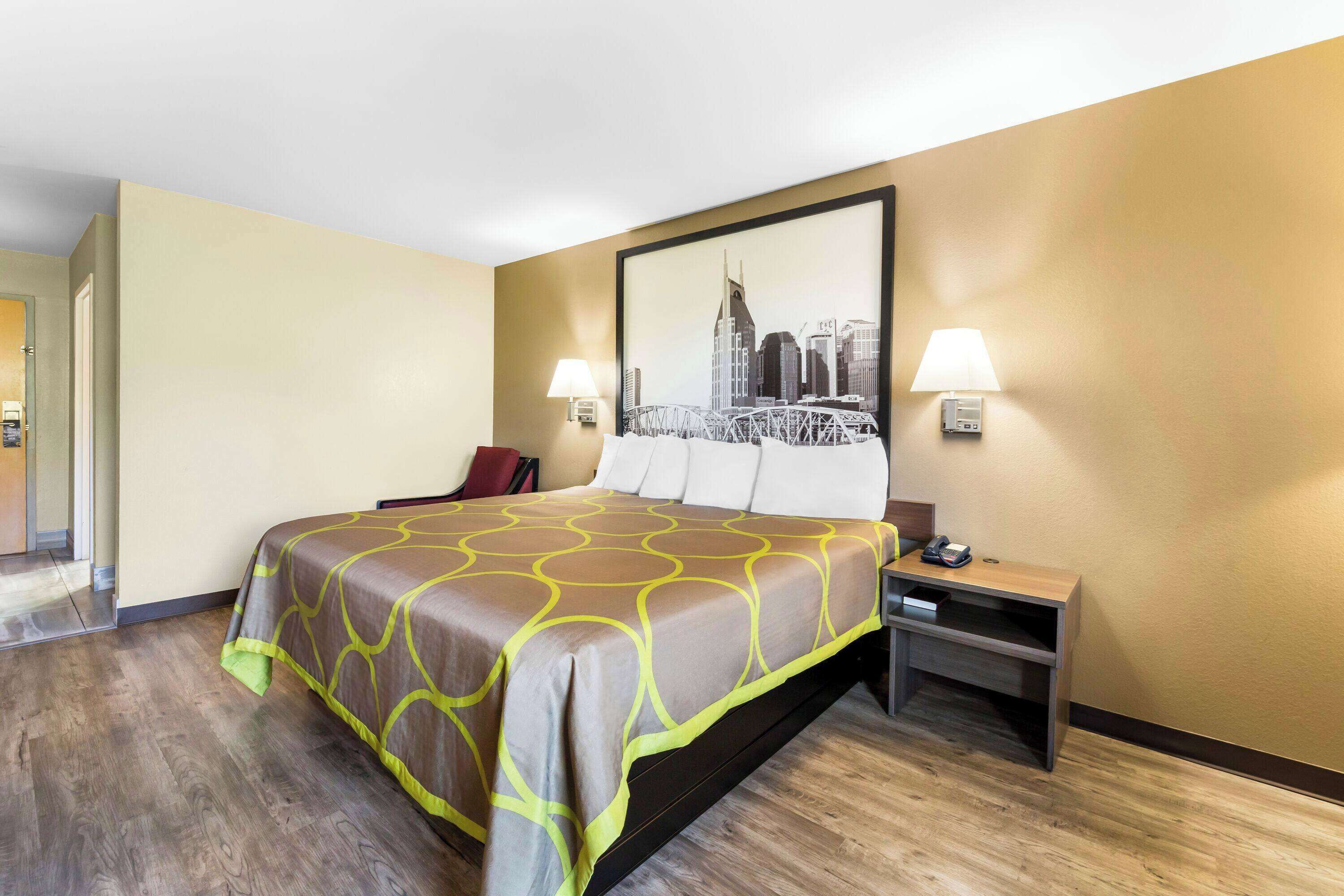 A hotel room with a bed, nightstand, and a framed cityscape picture on the wall.
