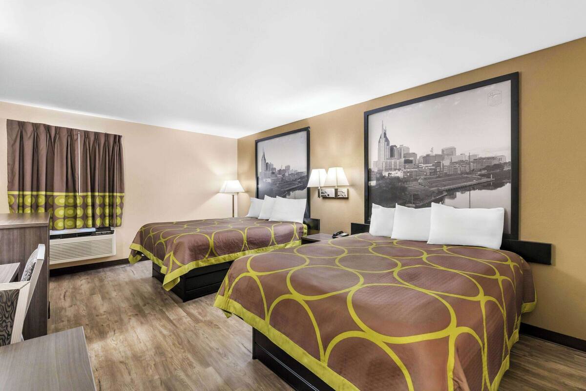 Habitación de hotel con dos camas, un escritorio y un cuadro de gran formato con una vista urbana.