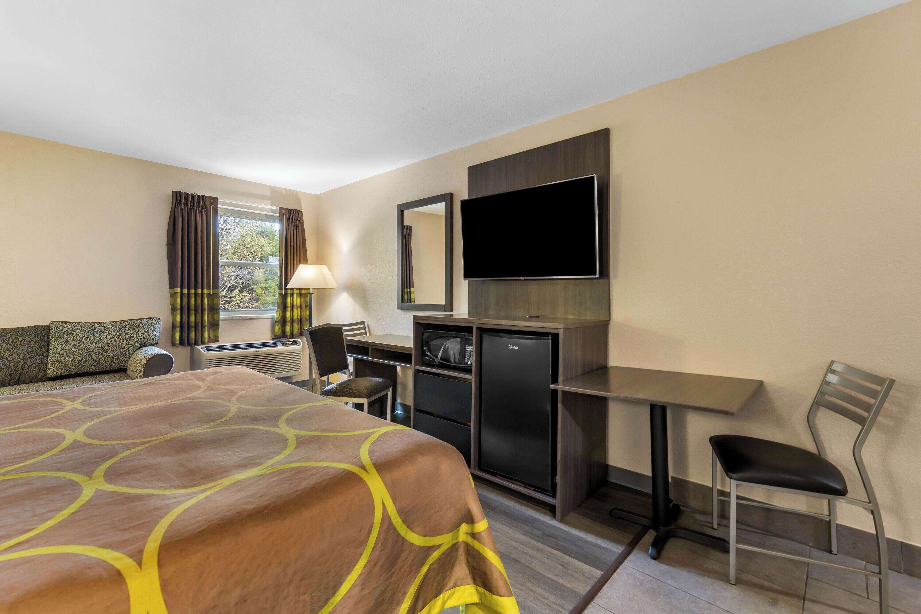 A hotel room with a large bed, a desk with a chair, a television, and a refrigerator.