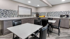 A modern kitchen with grey cabinets, a tiled backsplash, and a dining area with a table and chairs. - Super 8 by Wyndham Dickson (Dickson)