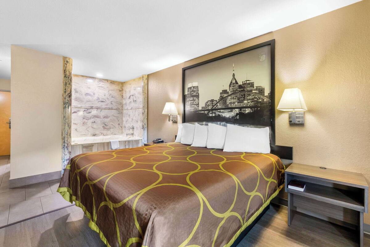 Habitación de hotel con una cama grande, un cuadro de paisaje urbano en la pared, un escritorio con lámpara y una mesita pequeña.