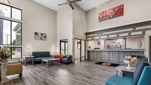 A spacious lobby with a high ceiling, a seating area with sofas and chairs, a reception desk, and a large window offering a view of the outdoors. - Super 8 by Wyndham Dickson (Dickson)