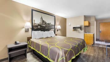 Quarto de hotel com cama, luminárias de cabeceira, mesa de cabeceira, escrivaninha, cadeira, cozinha compacta e porta.