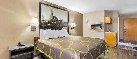 Une chambre d’hôtel comprenant un lit, des lampes de chevet, une table de chevet, un bureau, une chaise, un coin cuisine et une porte.