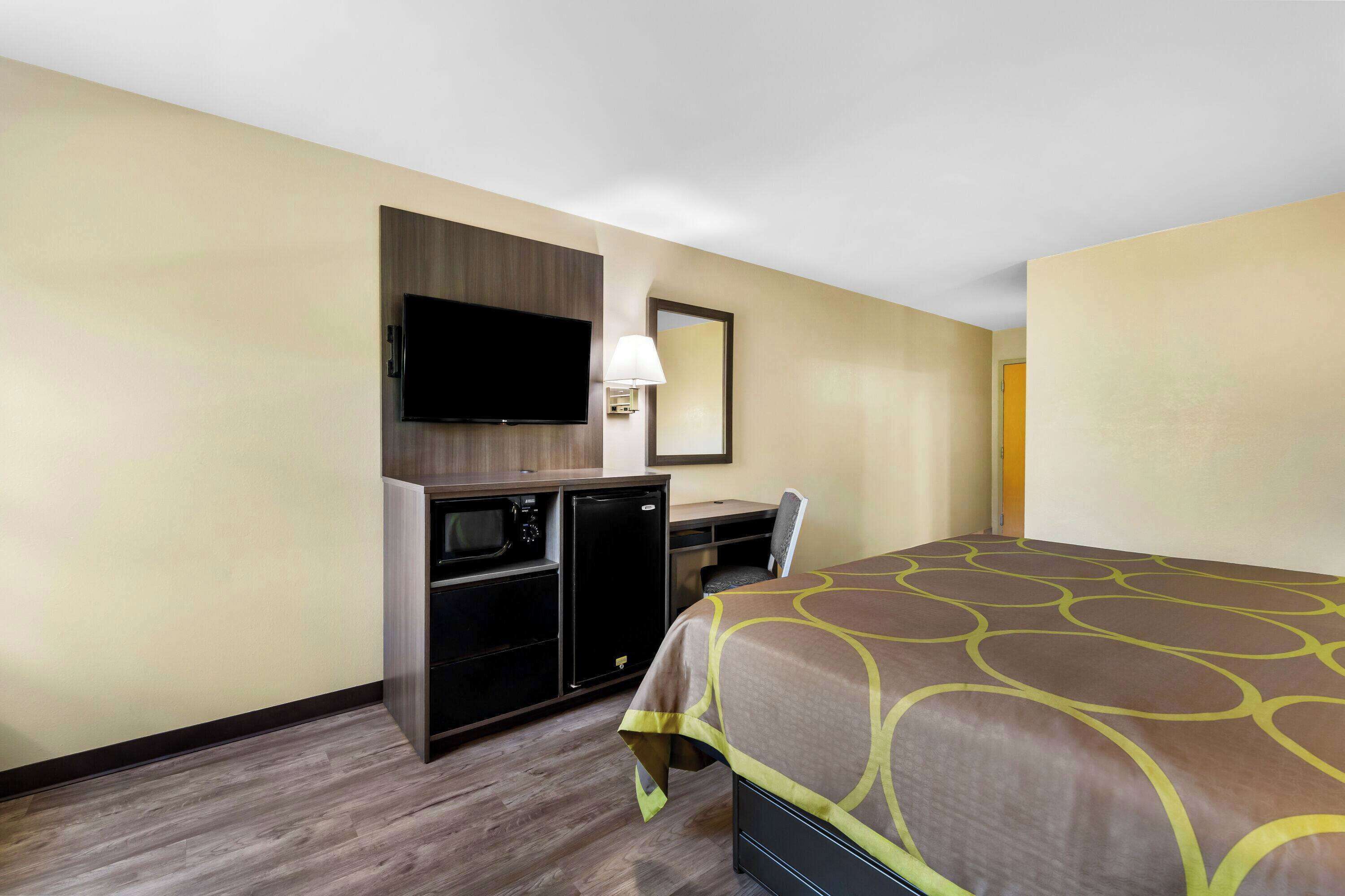 A hotel room with a bed, a desk with a chair, a television, and a microwave.