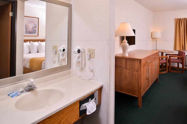 A hotel room with a large mirror, a sink, a wooden vanity, a chair, and a lamp. - Americas Best Value Inn Missouri Valley (Missouri Valley)