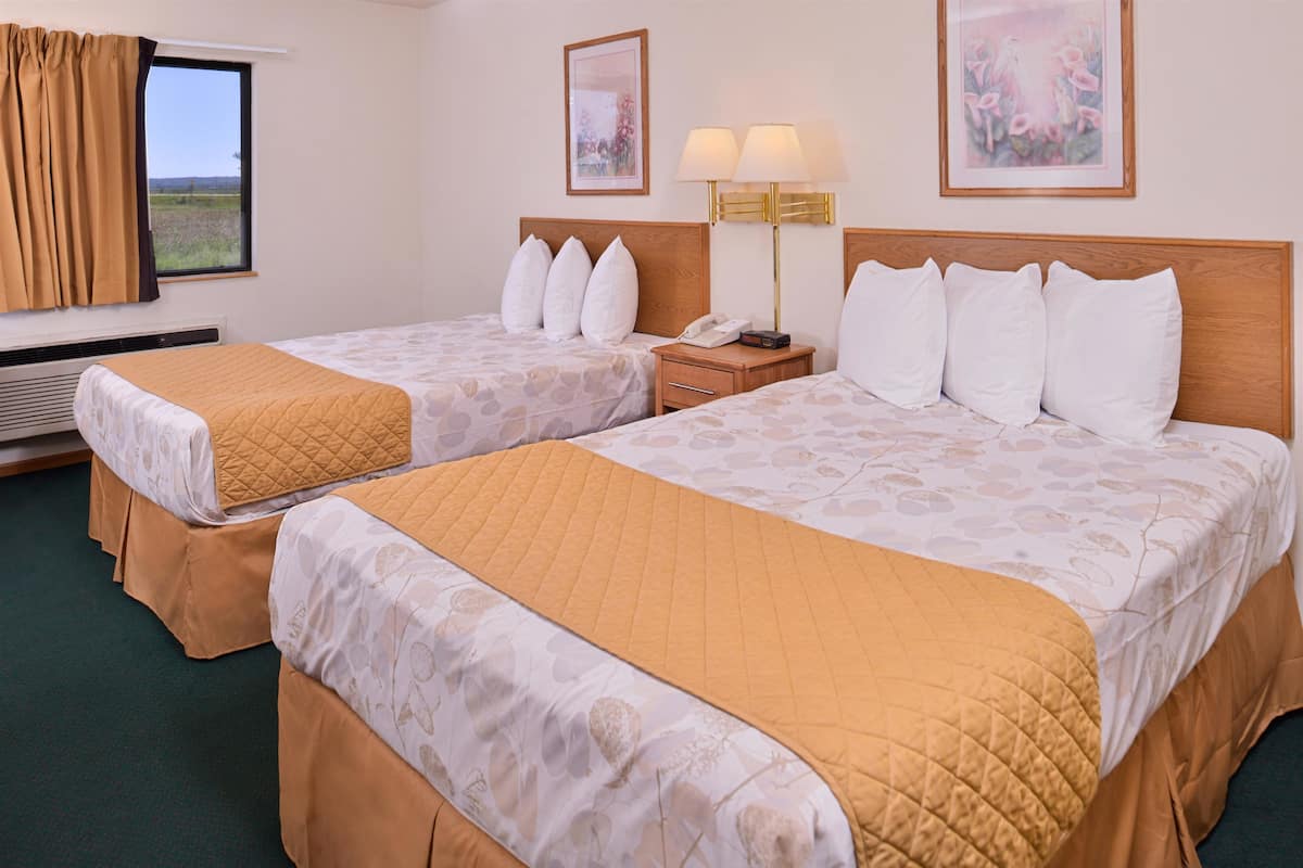 A hotel room with two beds, each with a quilted bedspread and pillows, a bedside table with a lamp, and a framed picture on the wall.