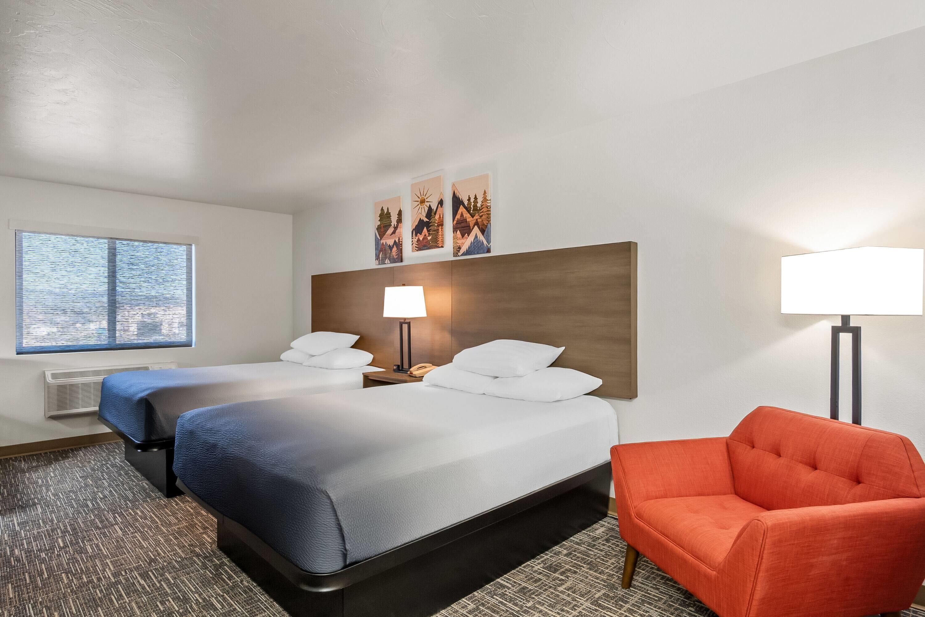 A hotel room with a large bed, two bedside tables, a chair, and a window with blinds.