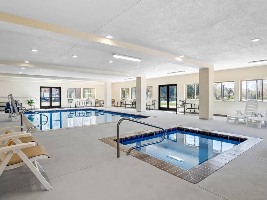 Una piscina interior con borde de azulejos, sillas de descanso y vistas al exterior a través de amplios ventanales.