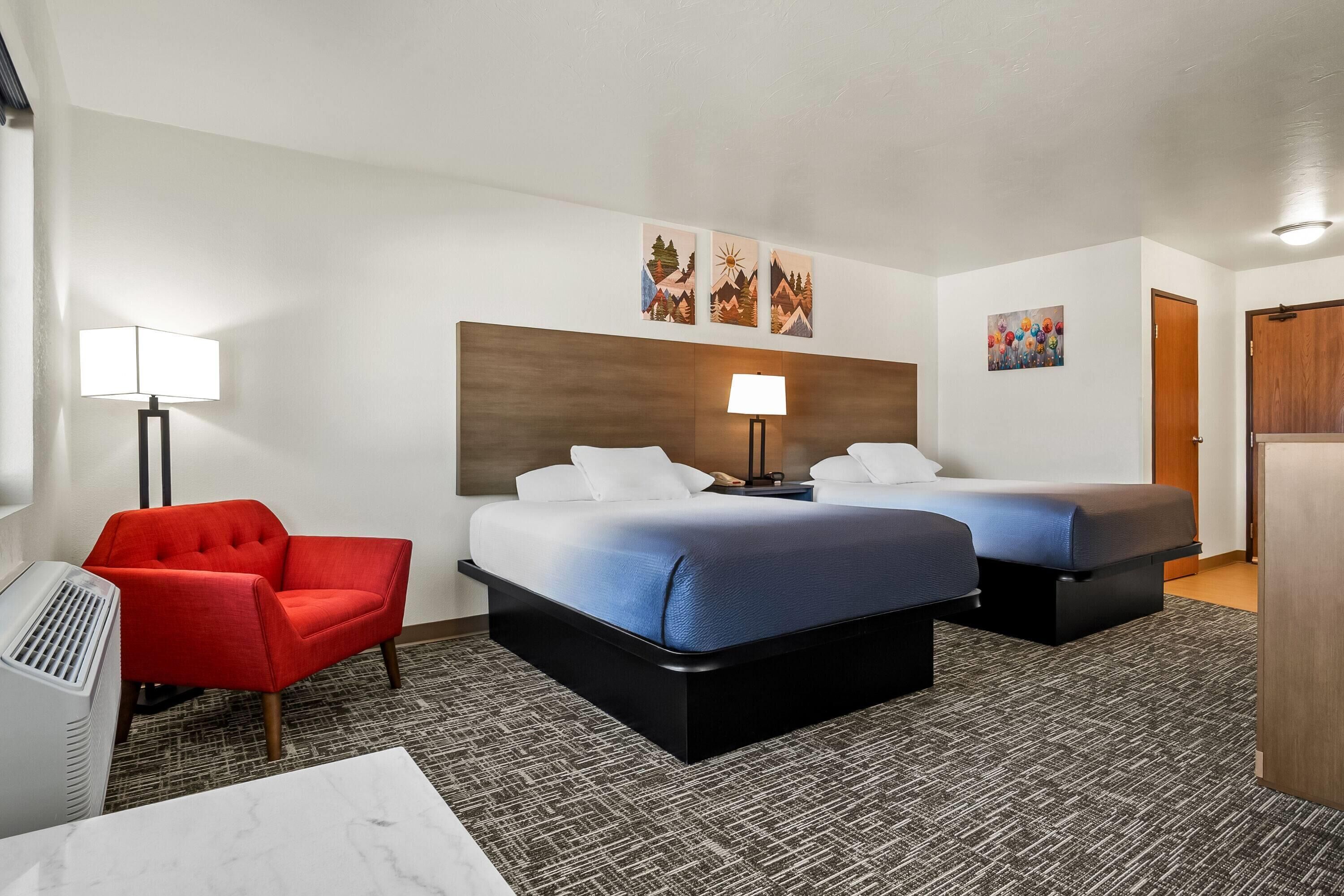 Une chambre d’hôtel avec deux lits, une chaise rouge, un bureau et une lampe.
