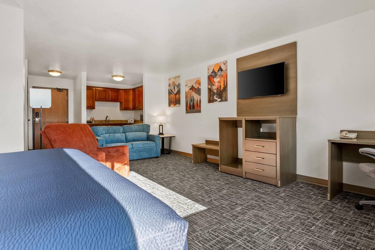 Habitación de hotel con cama, escritorio, silla, sofá, televisor y cocina.