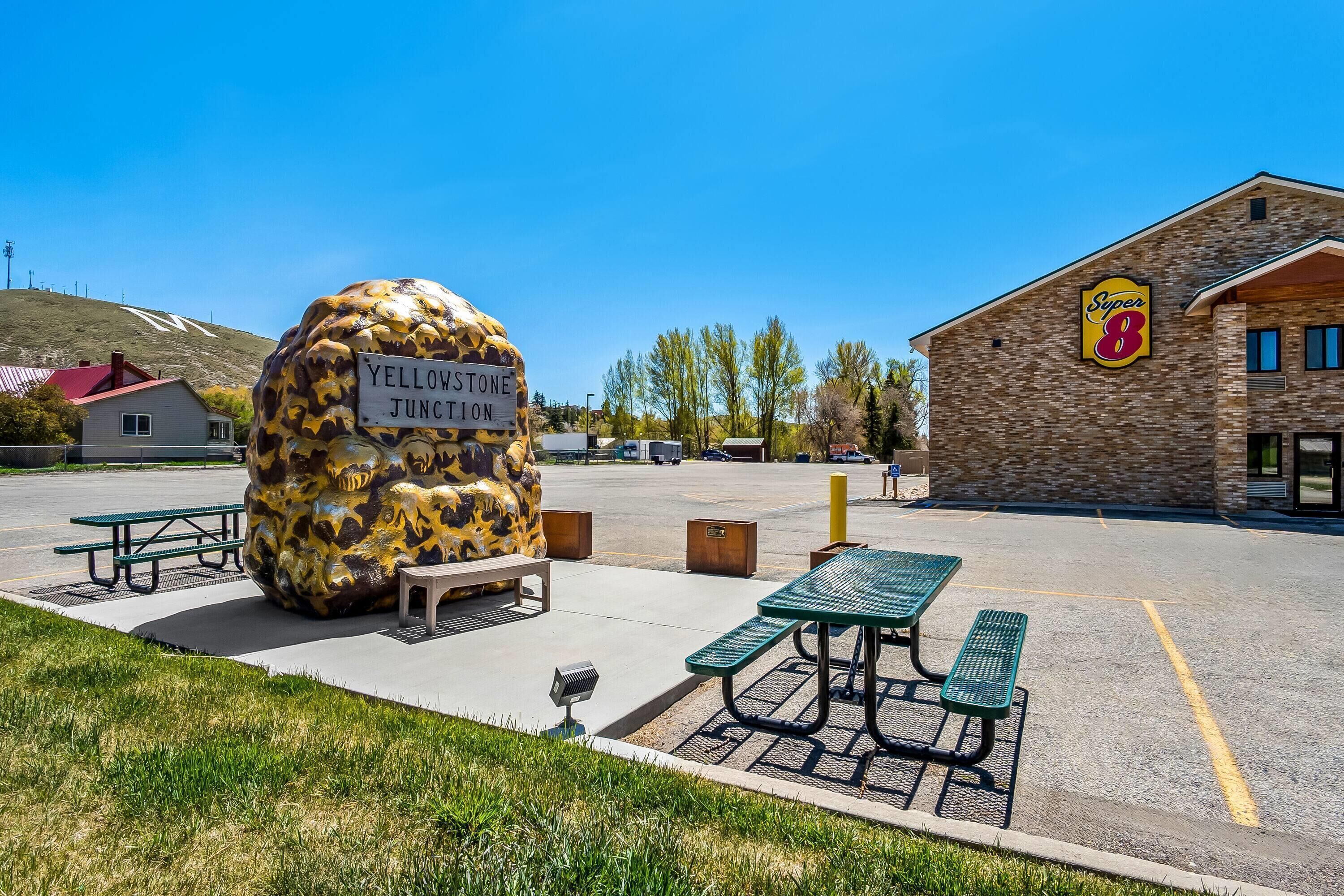 A parking lot with picnic tables, a large rock sculpture labeled 'Yellowstone Junction,' and a building with a 'Super 8' sign.