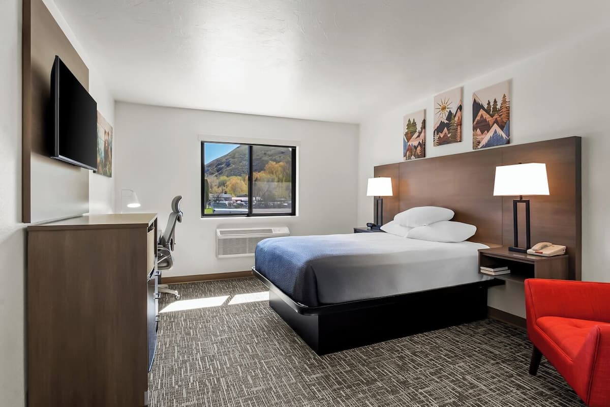 Habitación de hotel con cama, dos lámparas de noche, televisor, escritorio con silla y ventana con vista a la montaña.