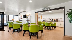 Een moderne eethoek met groene stoelen en een houten tafel, een keuken met een 'WELCOME' bord en een zicht door een deur.