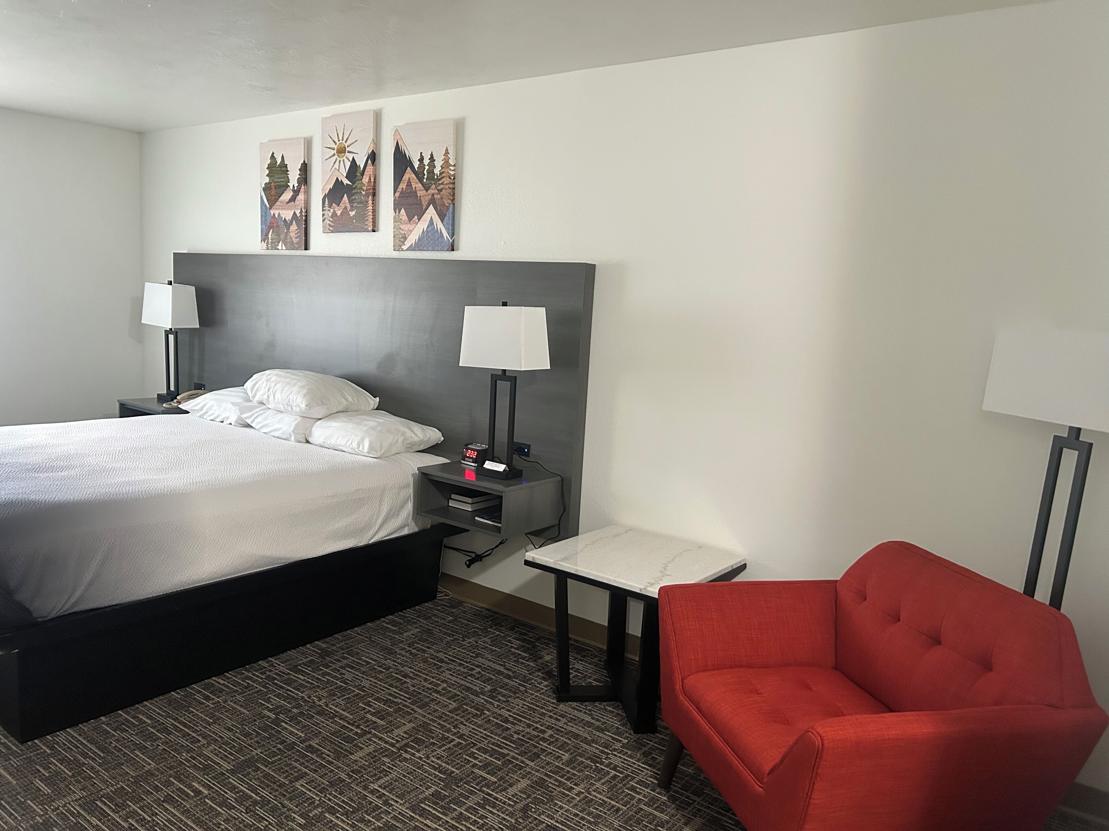 A hotel room with a bed, two bedside tables, a red chair, and artwork on the wall.