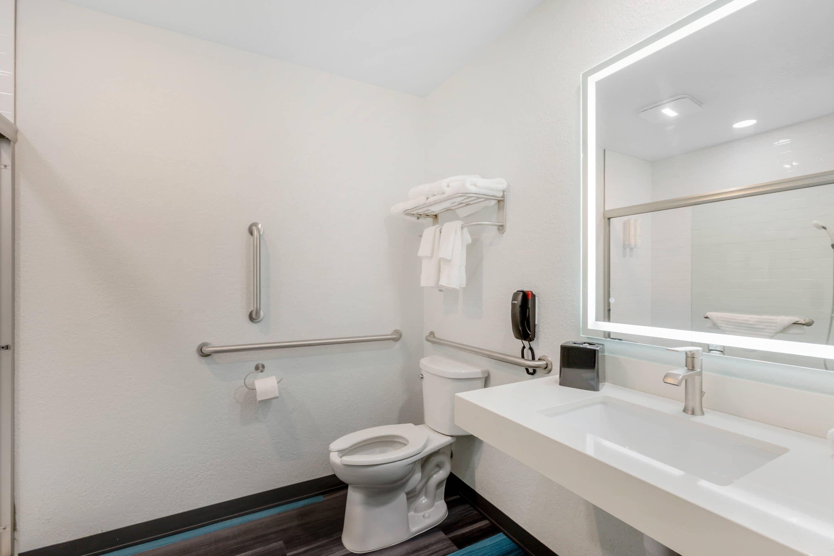 Un baño moderno con inodoro blanco, lavabo con espejo y zona de ducha.