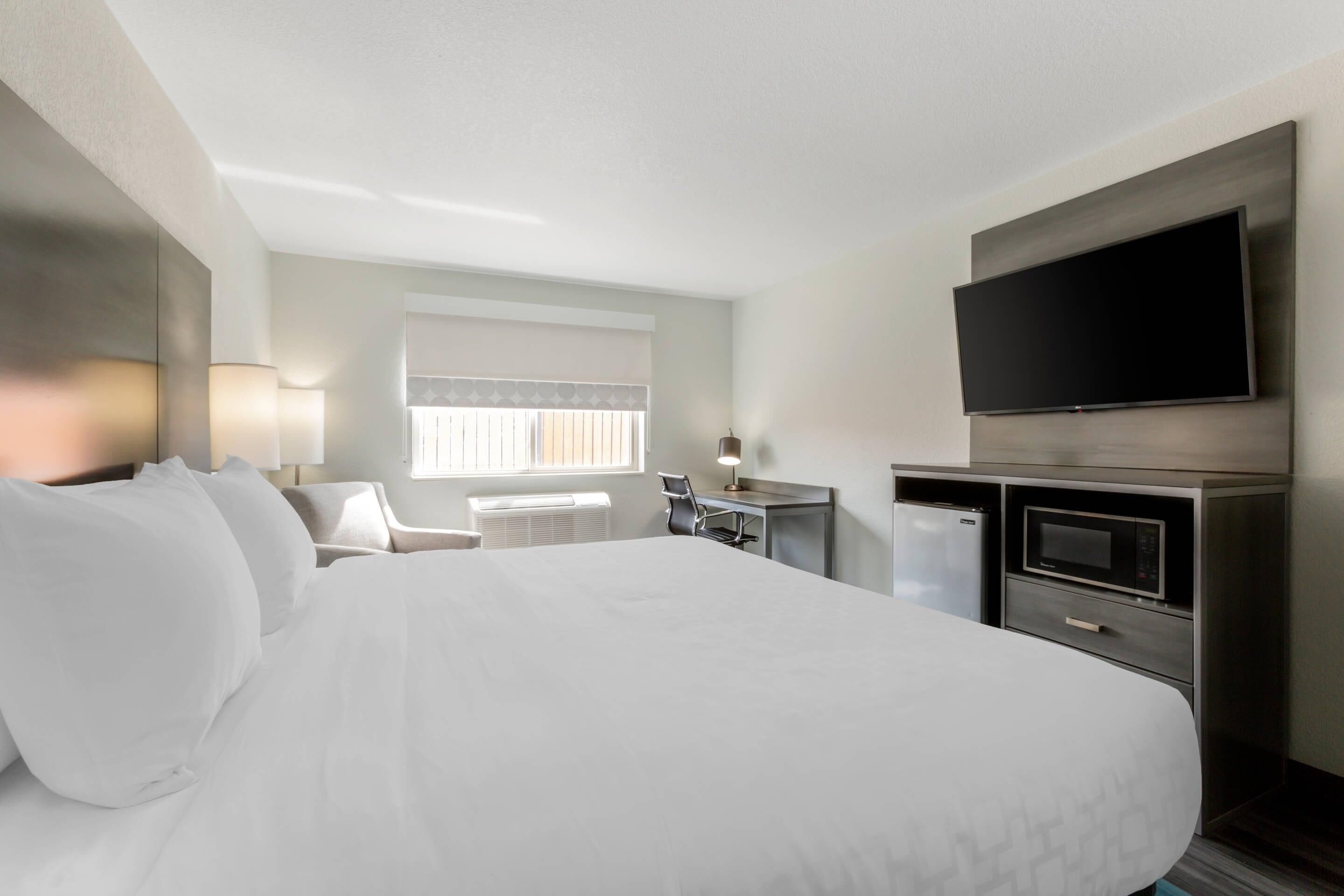A hotel room with a large bed, a desk with a computer, a flat-screen TV, and a microwave.