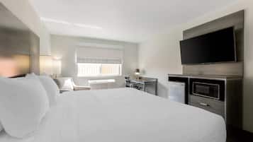 A hotel room with a large bed, a desk with a computer, a flat-screen TV, and a microwave.