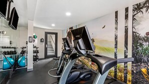 Uma academia com equipamentos de ginástica, um espelho e um mural na parede.