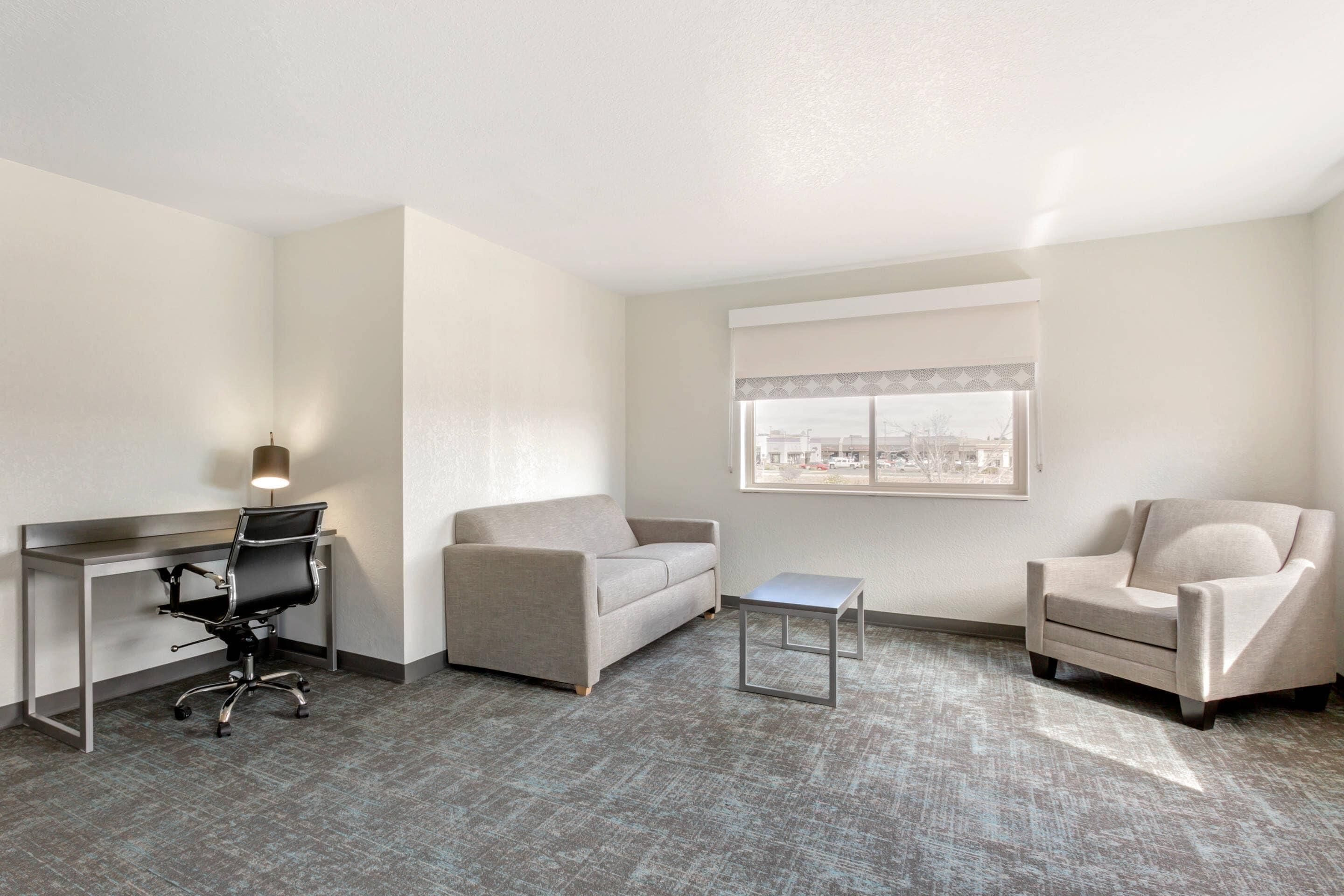 A hotel room with a desk, two armchairs, a small table, and a window with a view.