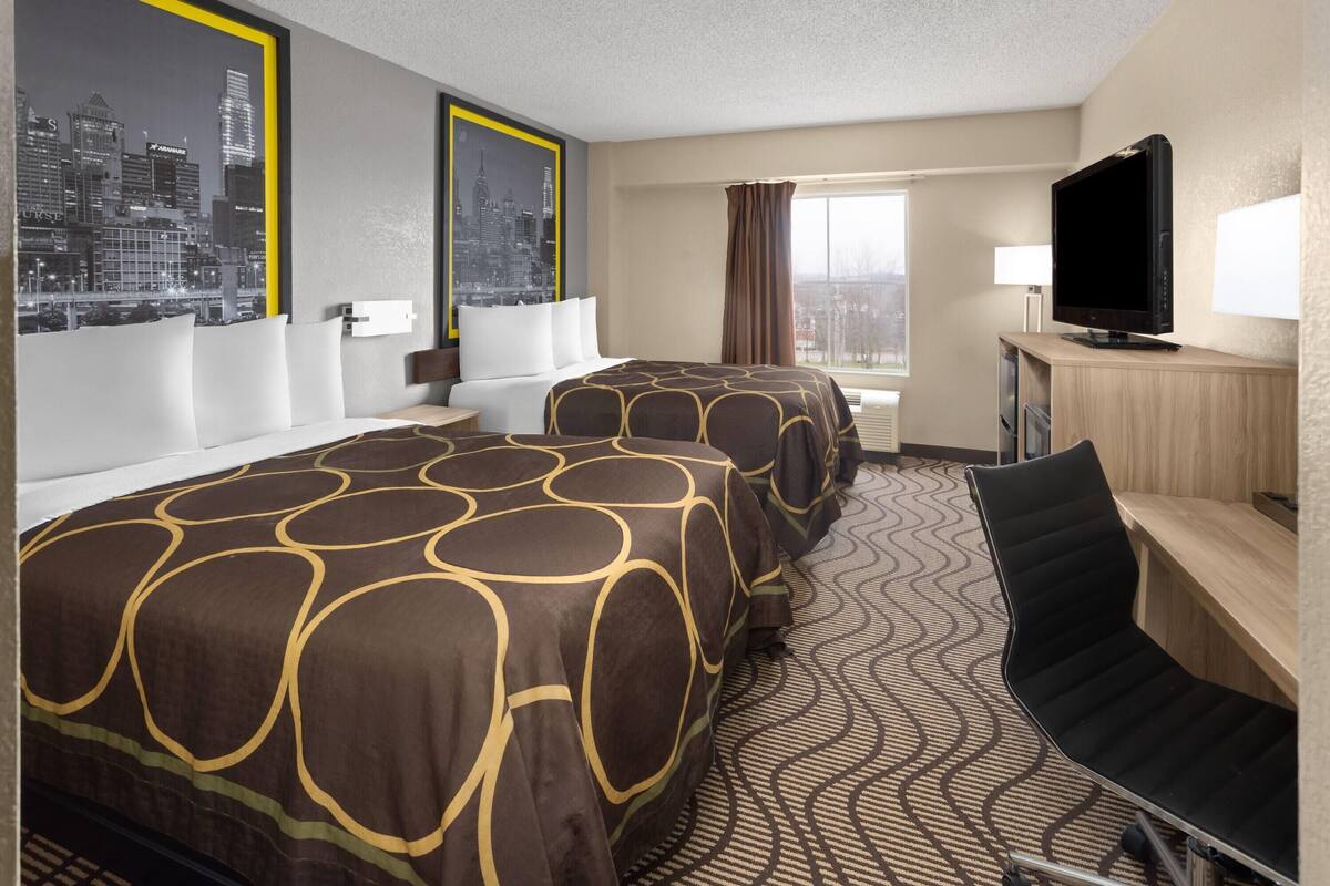 Een hotelkamer met twee bedden, een bureau met televisie, een stoel, een raam met gordijnen en uitzicht op de stad.