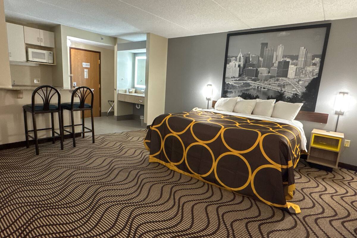 Een hotelkamer met een bed, een bureau met twee stoelen, een magnetron, een groot stadsgezicht poster en een nachtkastje met een lamp.