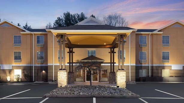 A multi-story hotel with a covered entrance, a parking lot, and a landscaped area with rocks. - Super 8 by Wyndham Mars/Cranberry/Pittsburgh Area (Mars)