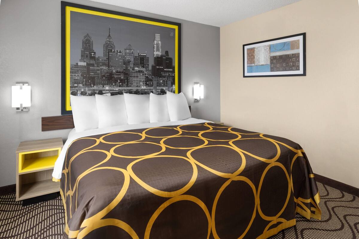 Hotelkamer met een bed, nachtkastje, wandlamp, stadsbeeld in een lijst en een kamerbreed tapijt met dessin.