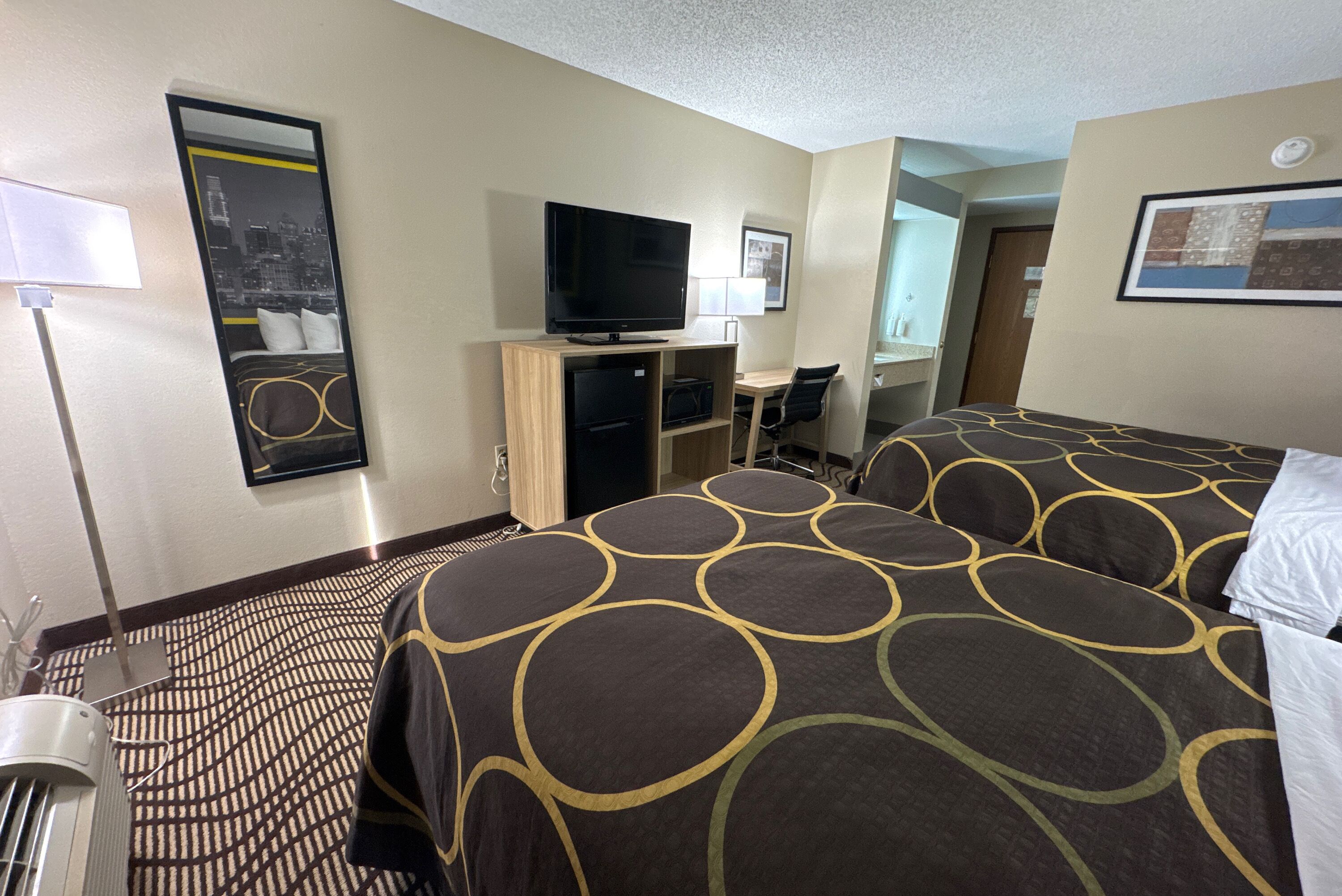Una habitación de hotel con una cama, un escritorio con computadora, un televisor y un espejo.