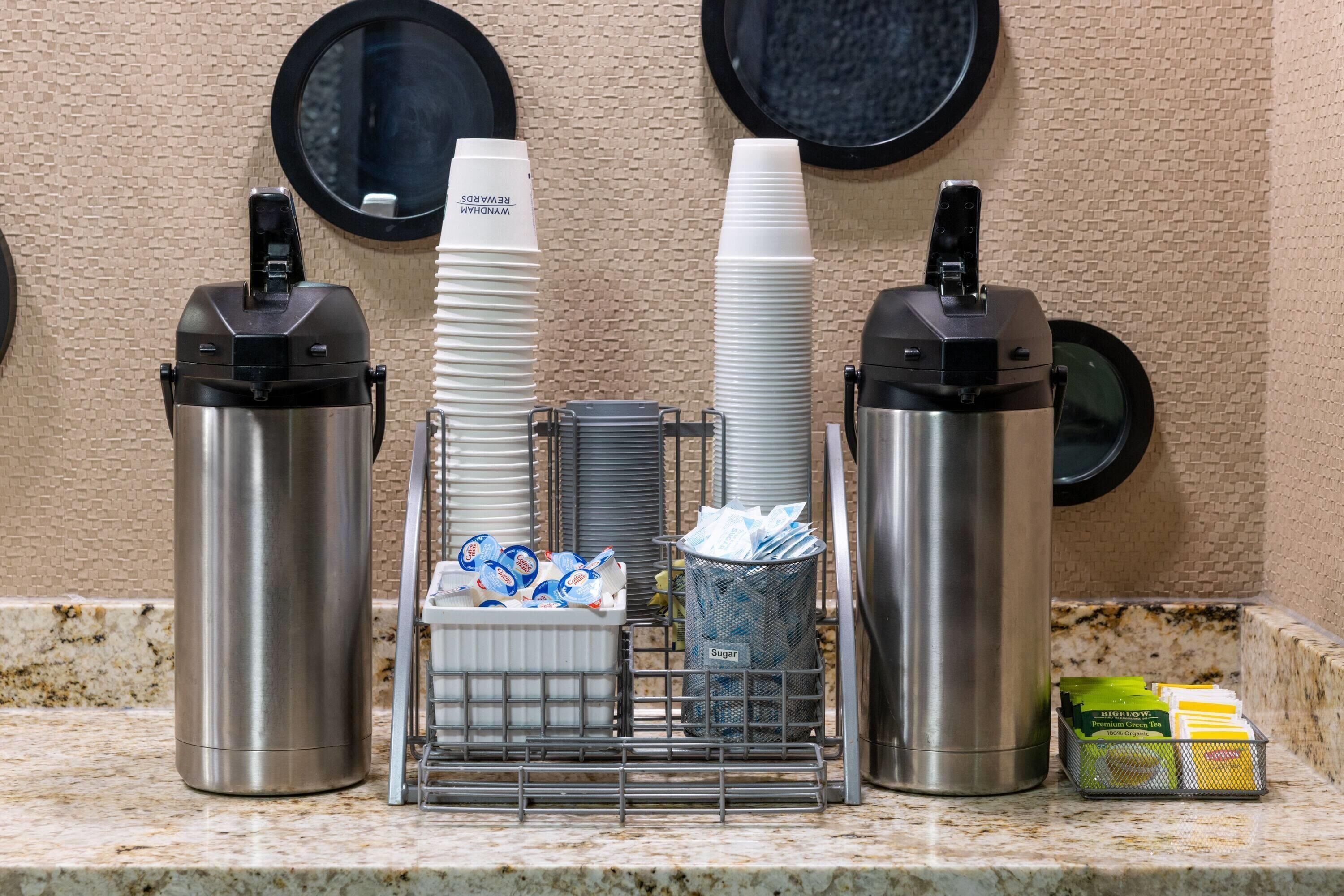 A self-service beverage station with disposable cups, a sugar container, and a basket of sugar packets.