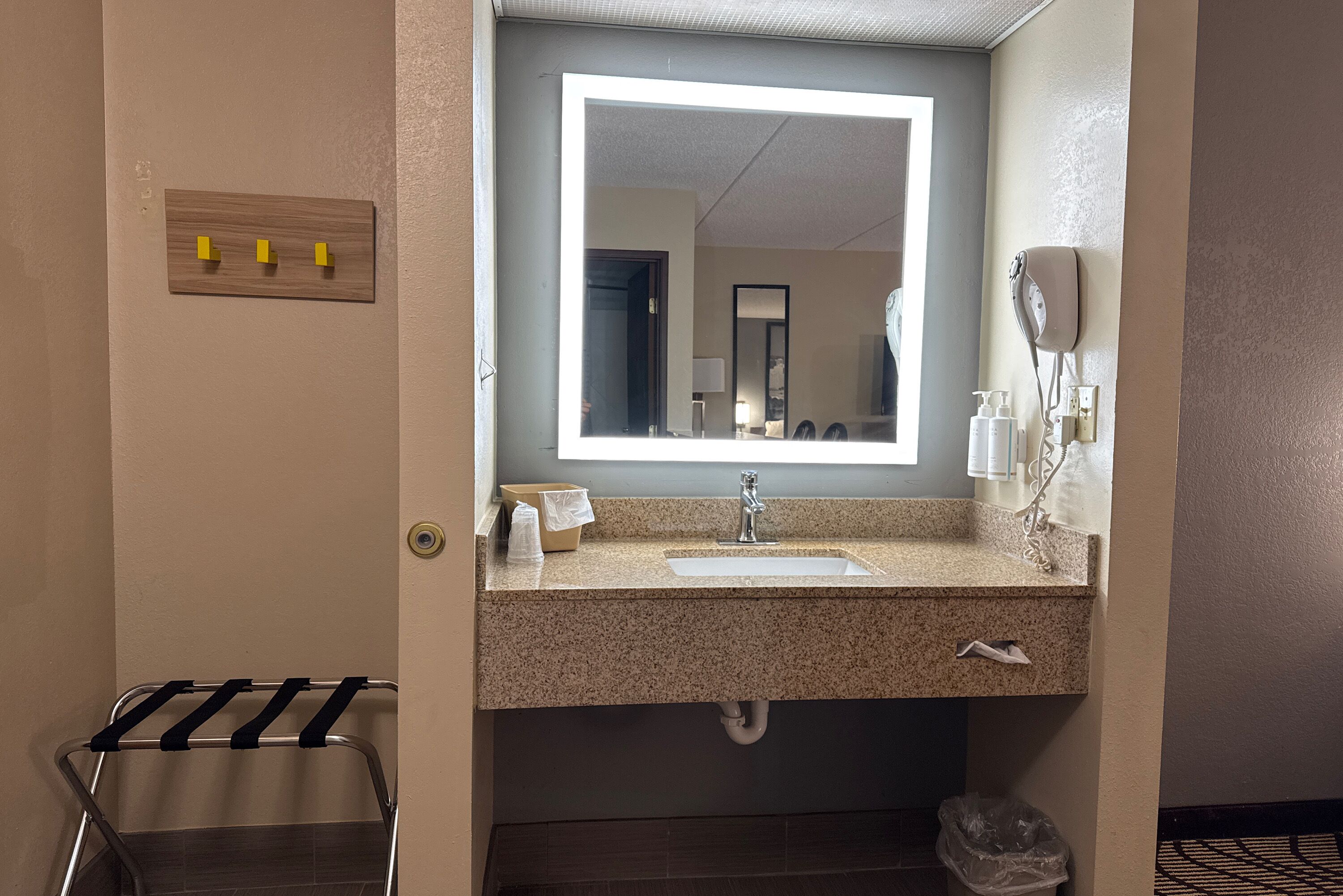 A bathroom with a sink, mirror, towel rack, and a trash bin.