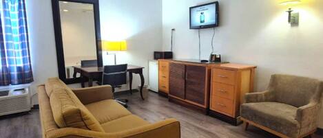 A living room with a sofa, armchair, TV, and a desk with a lamp.