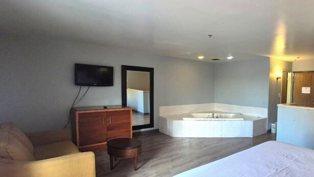A modern hotel room with a large bed, a wooden dresser, a flat-screen TV, a large mirror, and a separate bathroom with a bathtub. -  Kings Inn By OYO Calumet Park I-57 (Calumet Park)