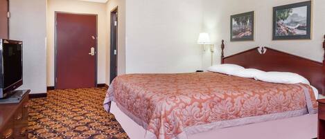 A hotel room with a large bed, a television, a door, and two framed pictures on the wall.