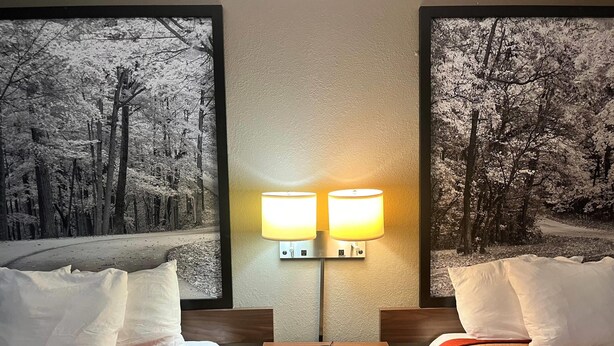 A hotel room with two beds, a nightstand, and a wall-mounted lamp. - Super 8 by Wyndham Evansville North (Evansville)