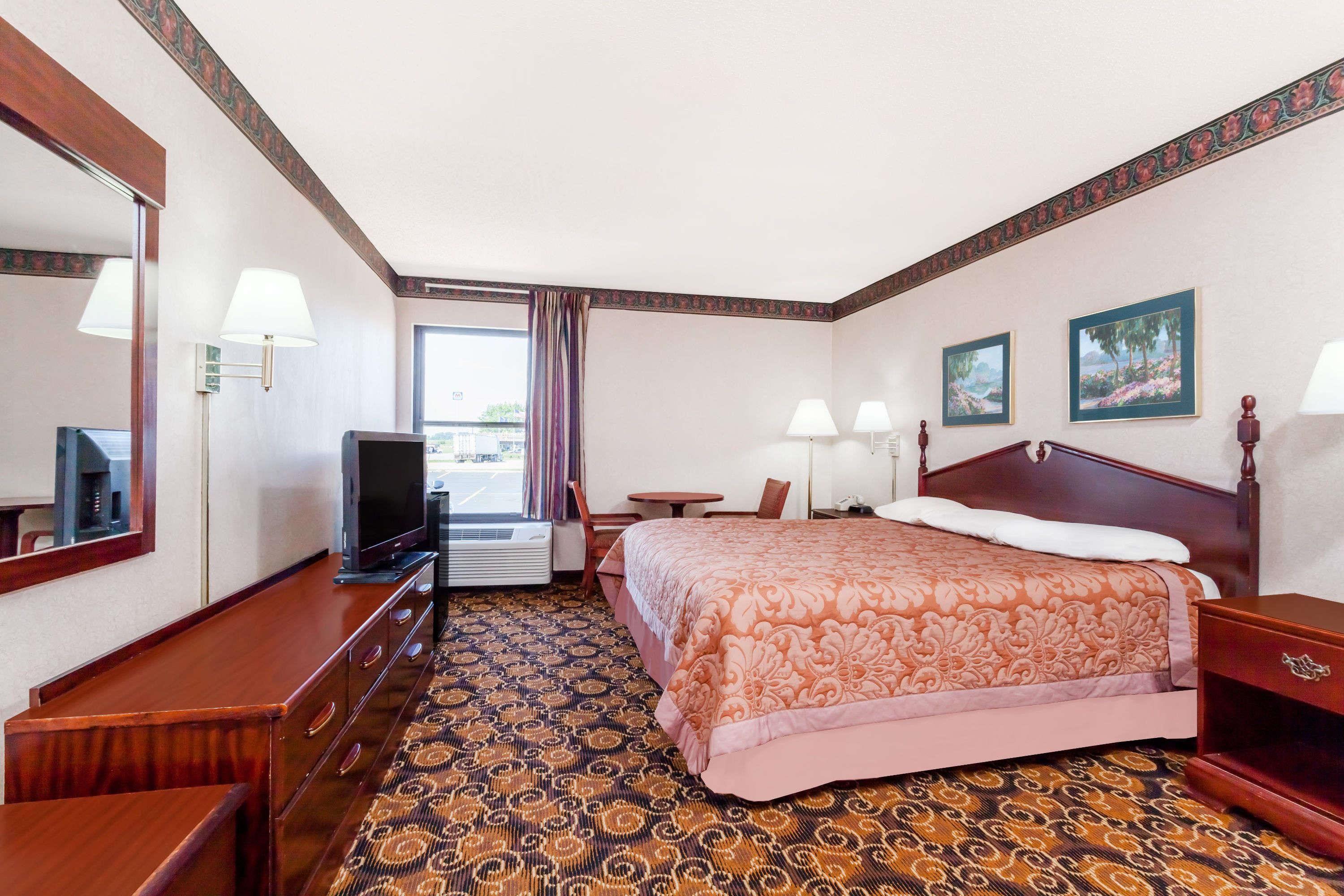 A hotel room with a bed, a TV, a desk, a chair, and a window.