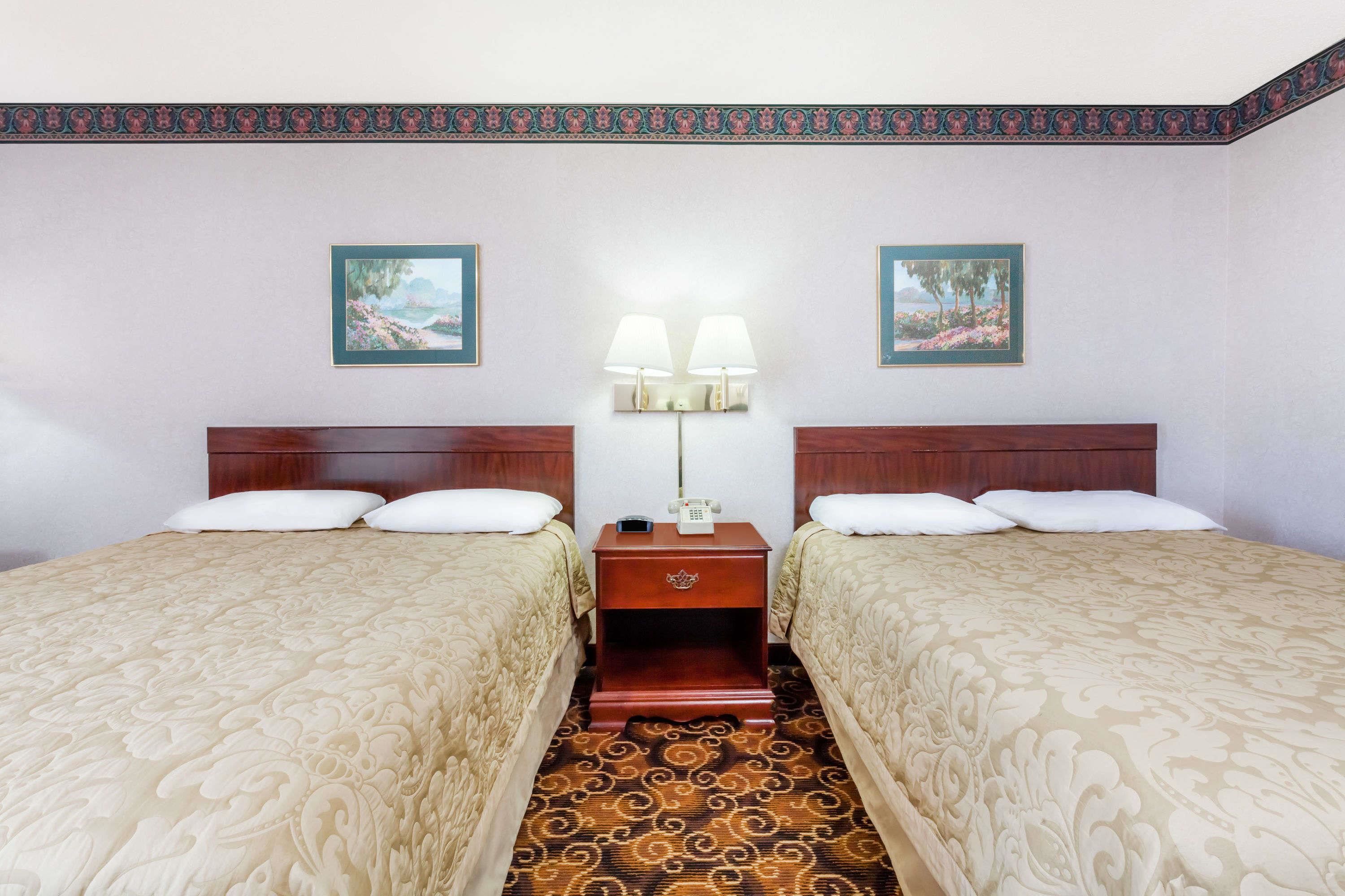 A hotel room with two beds, a nightstand with a lamp, and two framed pictures on the wall.