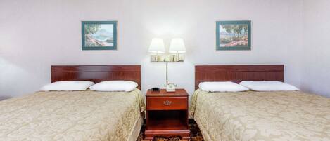 A hotel room with two beds, a nightstand with a lamp, and two framed pictures on the wall.
